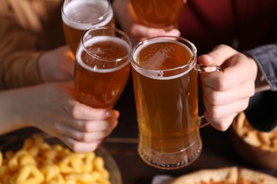 Photo of Friends clinking glasses of beer at table, closeup