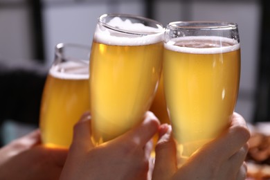 Photo of Friends clinking glasses of beer indoors, closeup