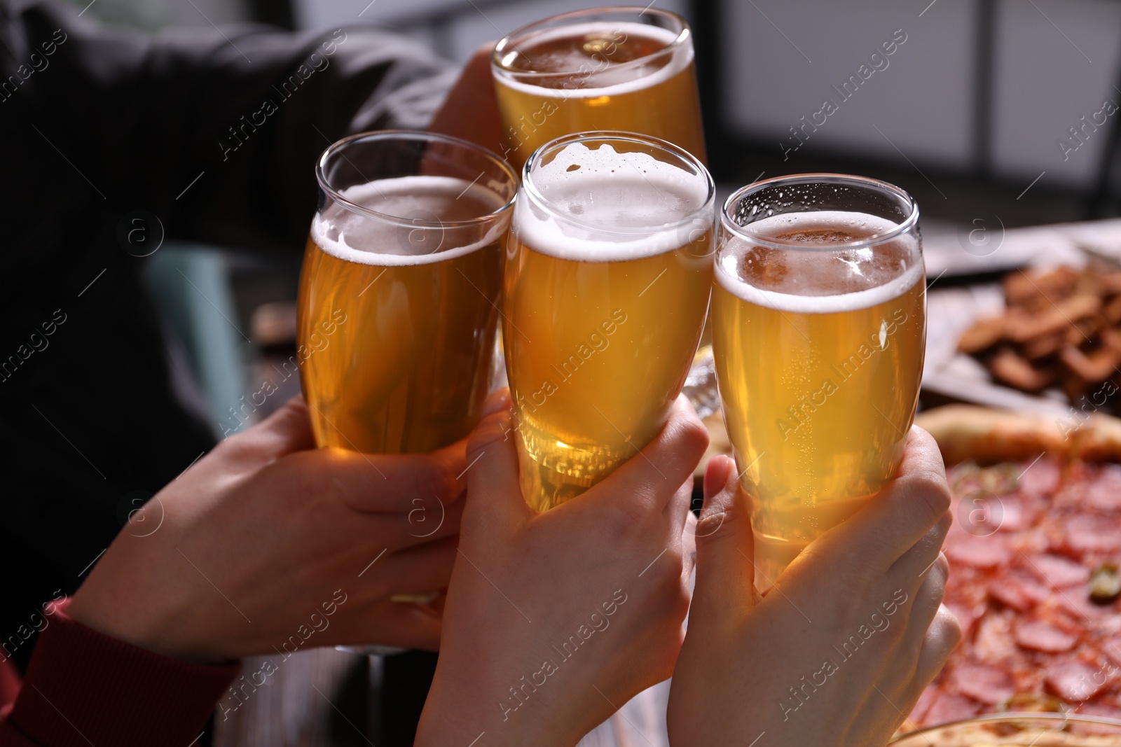 Friends clinking glasses of beer at table, closeup Photo of Friends clinking glasses of beer at table, closeup