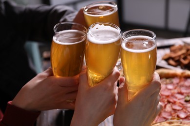 Photo of Friends clinking glasses of beer at table, closeup