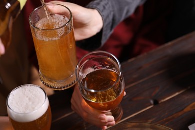 Photo of Pouring beer into woman's glass at wooden table, closeup