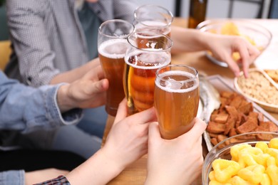 Photo of Friends clinking glasses of beer at wooden table, closeup