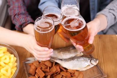 Photo of Friends clinking glasses of beer at wooden table, closeup