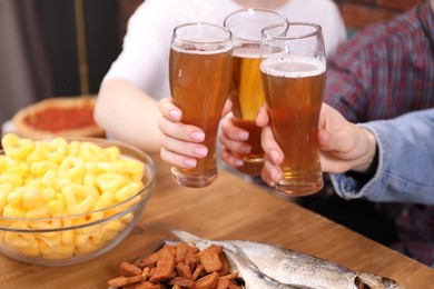 Photo of Friends clinking glasses of beer at wooden table, closeup