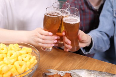 Photo of Friends clinking glasses of beer at wooden table, closeup
