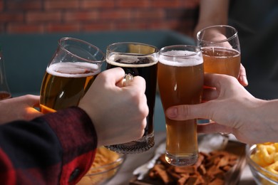 Photo of Friends clinking glasses of beer indoors, closeup