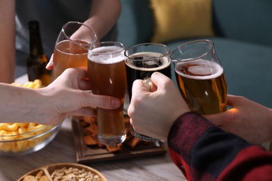 Photo of Friends clinking glasses of beer at white wooden table, closeup