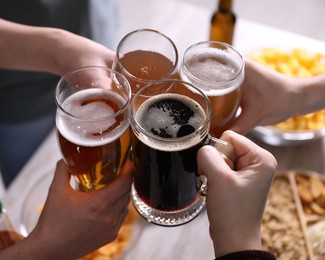 Photo of Friends clinking glasses of beer at table, closeup