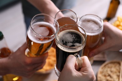 Photo of Friends clinking glasses of beer at table, closeup