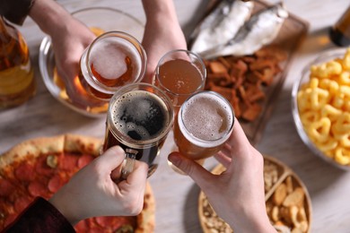 Photo of Friends clinking glasses of beer at white wooden table, top view