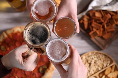 Photo of Friends clinking glasses of beer at white wooden table, top view