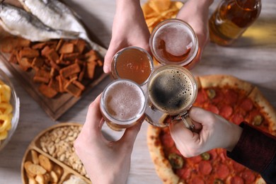 Photo of Friends clinking glasses of beer at white wooden table, top view