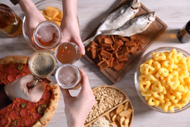 Photo of Friends clinking glasses of beer at white wooden table, top view