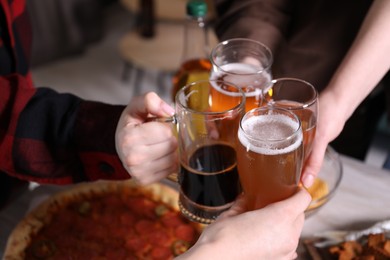 Photo of Friends clinking glasses of beer at white wooden table, closeup