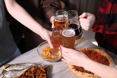Photo of Friends clinking glasses of beer at white wooden table, closeup