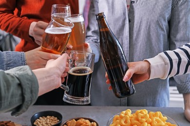 Photo of Friends clinking glasses of beer at table, closeup
