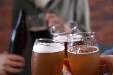 Photo of Friends clinking glasses of beer indoors, closeup