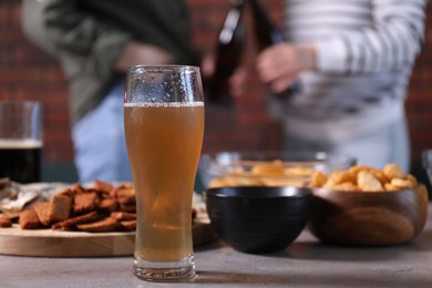 Photo of Glass of beer with snacks on table and friends chatting indoors, selective focus