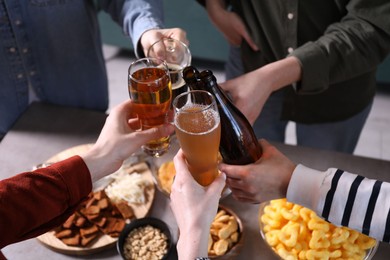 Photo of Friends clinking glasses of beer at table, closeup