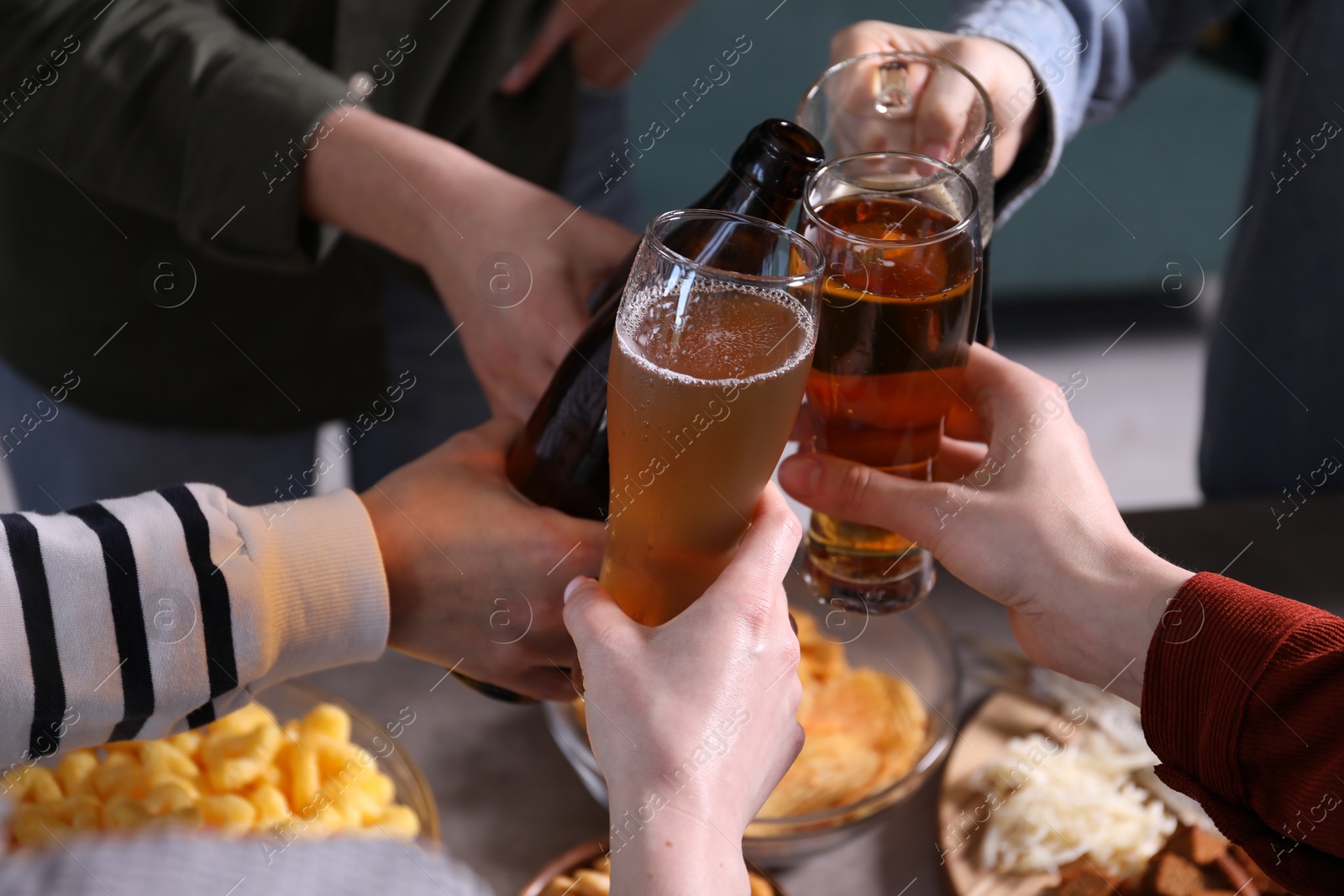 Friends clinking glasses of beer at table, closeup Photo of Friends clinking glasses of beer at table, closeup