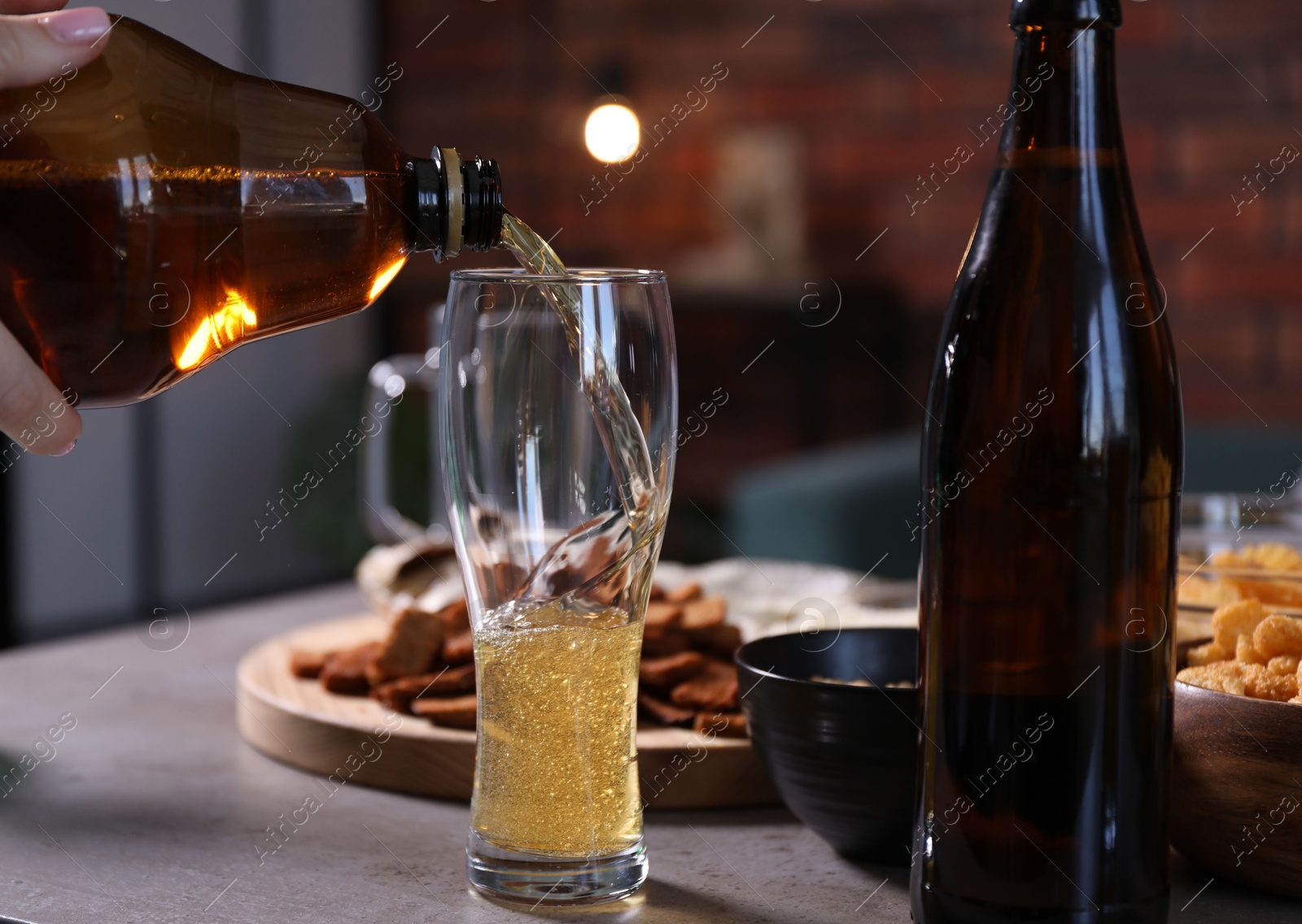 Woman pouring beer into glass at grey table, closeup Photo of Woman pouring beer into glass at grey table, closeup