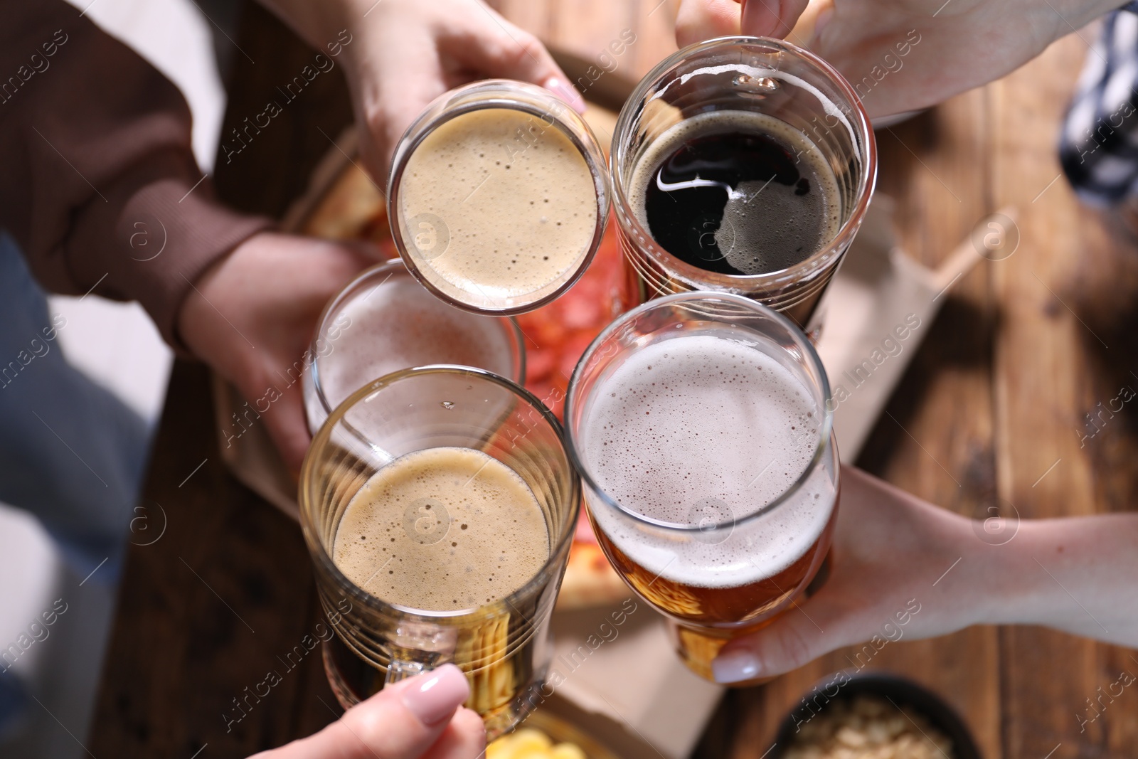 Friends clinking glasses of beer at table, closeup Photo of Friends clinking glasses of beer at table, closeup