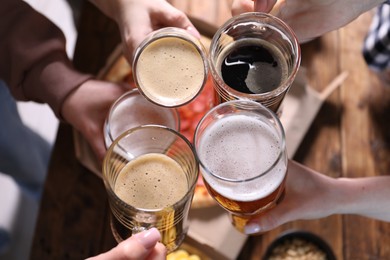 Photo of Friends clinking glasses of beer at table, closeup