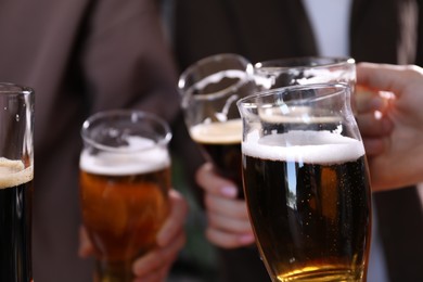Photo of Friends clinking glasses of beer indoors, closeup