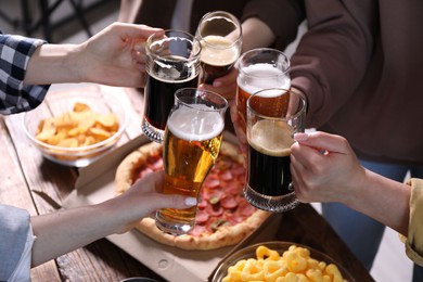 Photo of Friends clinking glasses of beer at table, closeup