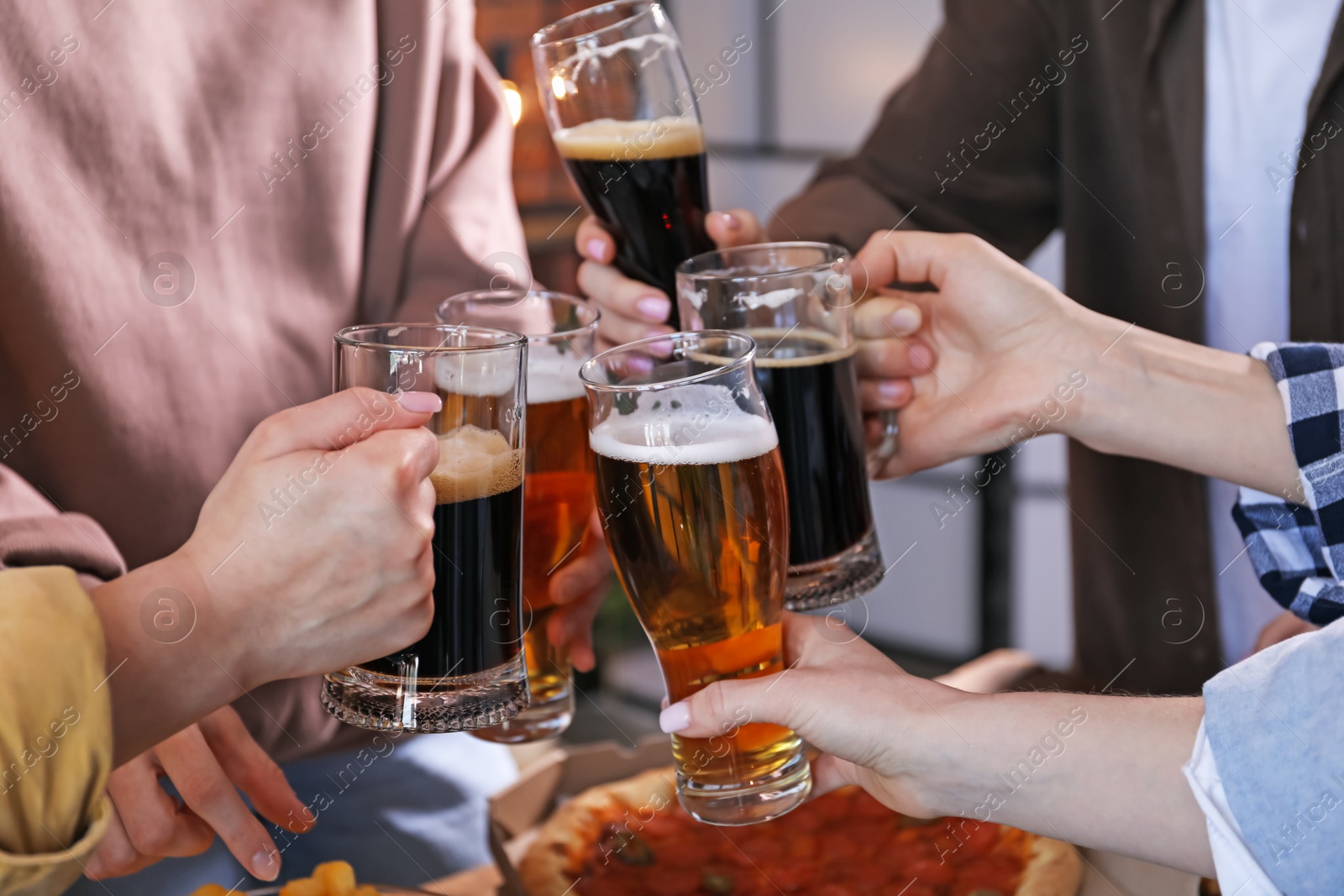 Friends clinking glasses of beer at table, closeup Photo of Friends clinking glasses of beer at table, closeup
