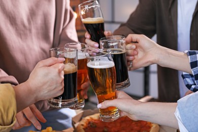 Photo of Friends clinking glasses of beer at table, closeup
