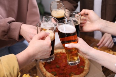 Photo of Friends clinking glasses of beer at table, closeup