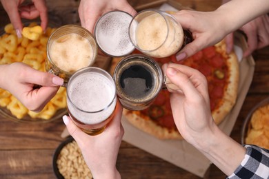 Photo of Friends clinking glasses of beer at wooden table, top view