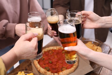 Photo of Friends clinking glasses of beer at wooden table, closeup