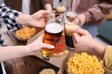 Photo of Friends clinking glasses of beer at wooden table, closeup