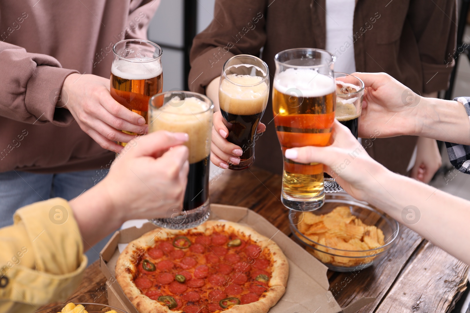 Friends clinking glasses of beer at wooden table, closeup Photo of Friends clinking glasses of beer at wooden table, closeup