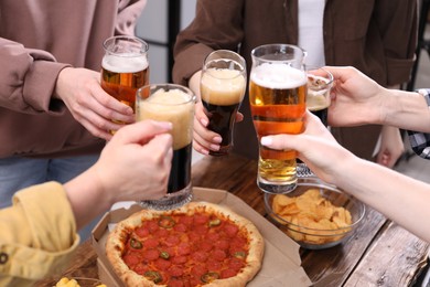 Photo of Friends clinking glasses of beer at wooden table, closeup