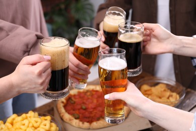 Photo of Friends clinking glasses of beer at wooden table, closeup
