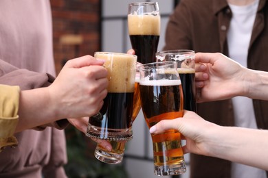 Photo of Friends clinking glasses of beer indoors, closeup