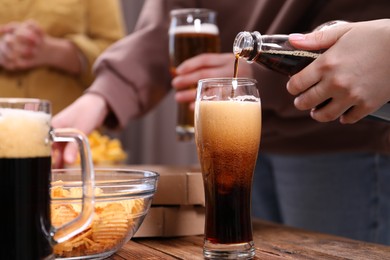Photo of Woman pouring beer into glass at wooden table, closeup