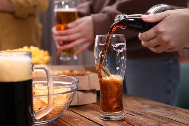 Photo of Woman pouring beer into glass at wooden table, closeup