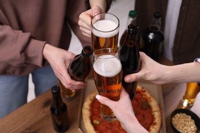 Photo of Friends clinking glasses of beer at wooden table, closeup