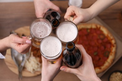 Photo of Friends clinking glasses of beer at wooden table, top view