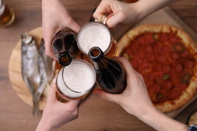 Photo of Friends clinking glasses of beer at wooden table, top view
