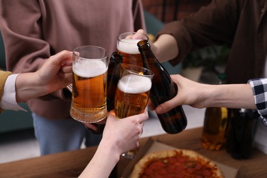 Photo of Friends clinking glasses of beer at table, closeup