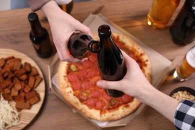 Photo of Friends clinking bottles of beer at wooden table, closeup