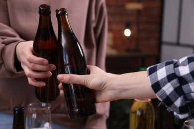 Photo of Friends clinking bottles of beer indoors, closeup
