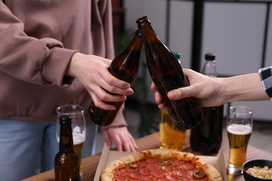 Photo of Friends clinking bottles of beer indoors, closeup