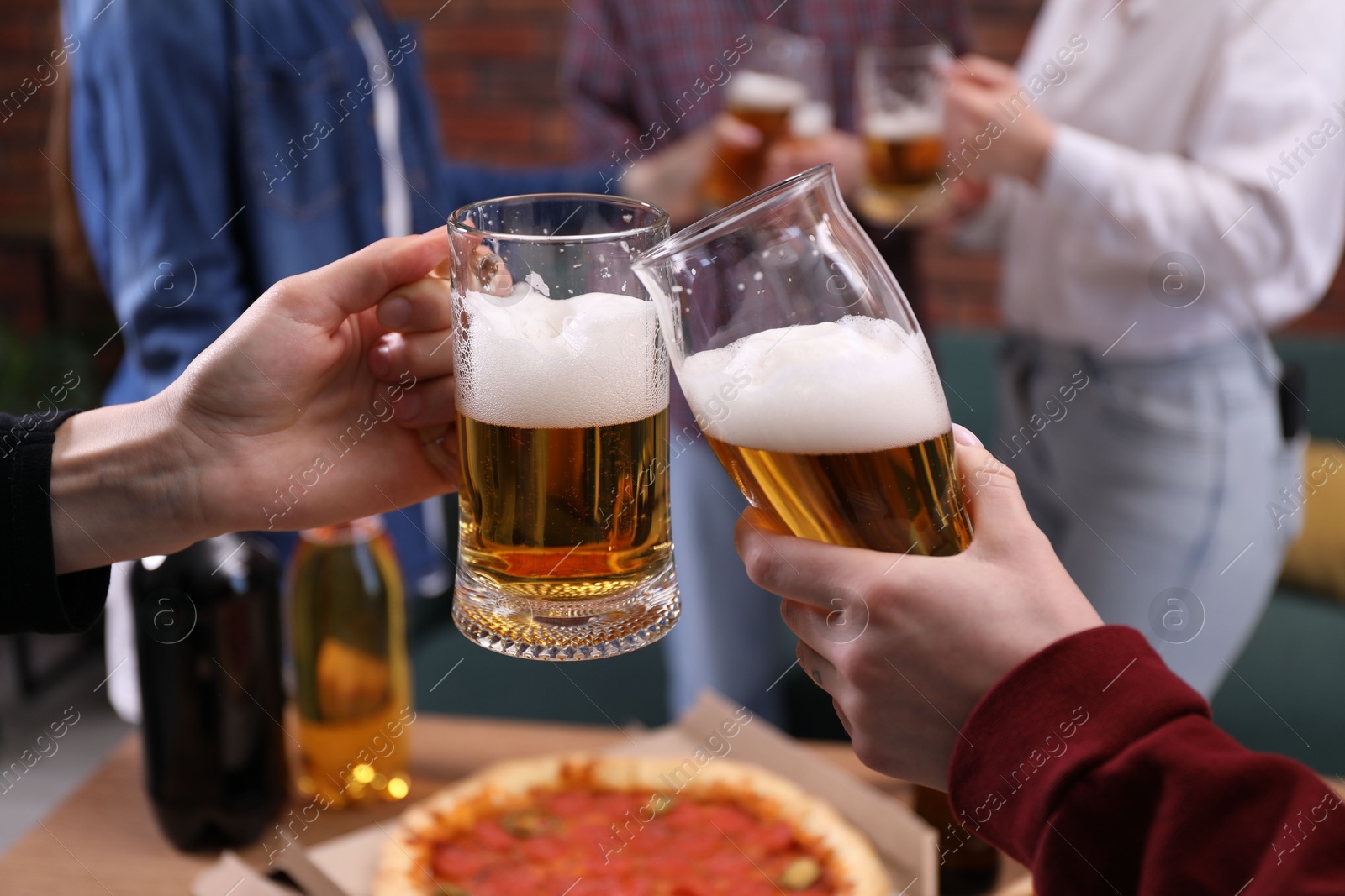 Friends clinking glasses of beer at table, closeup Photo of Friends clinking glasses of beer at table, closeup