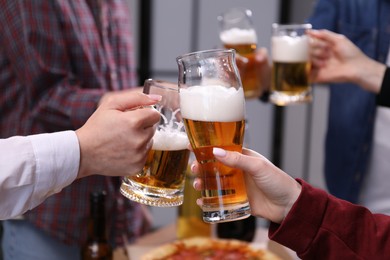 Photo of Friends clinking glasses of beer indoors, closeup